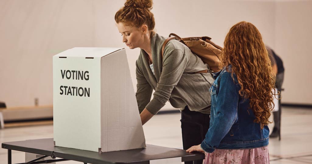 A woman votes at a polling station with her younger daughter by her side.